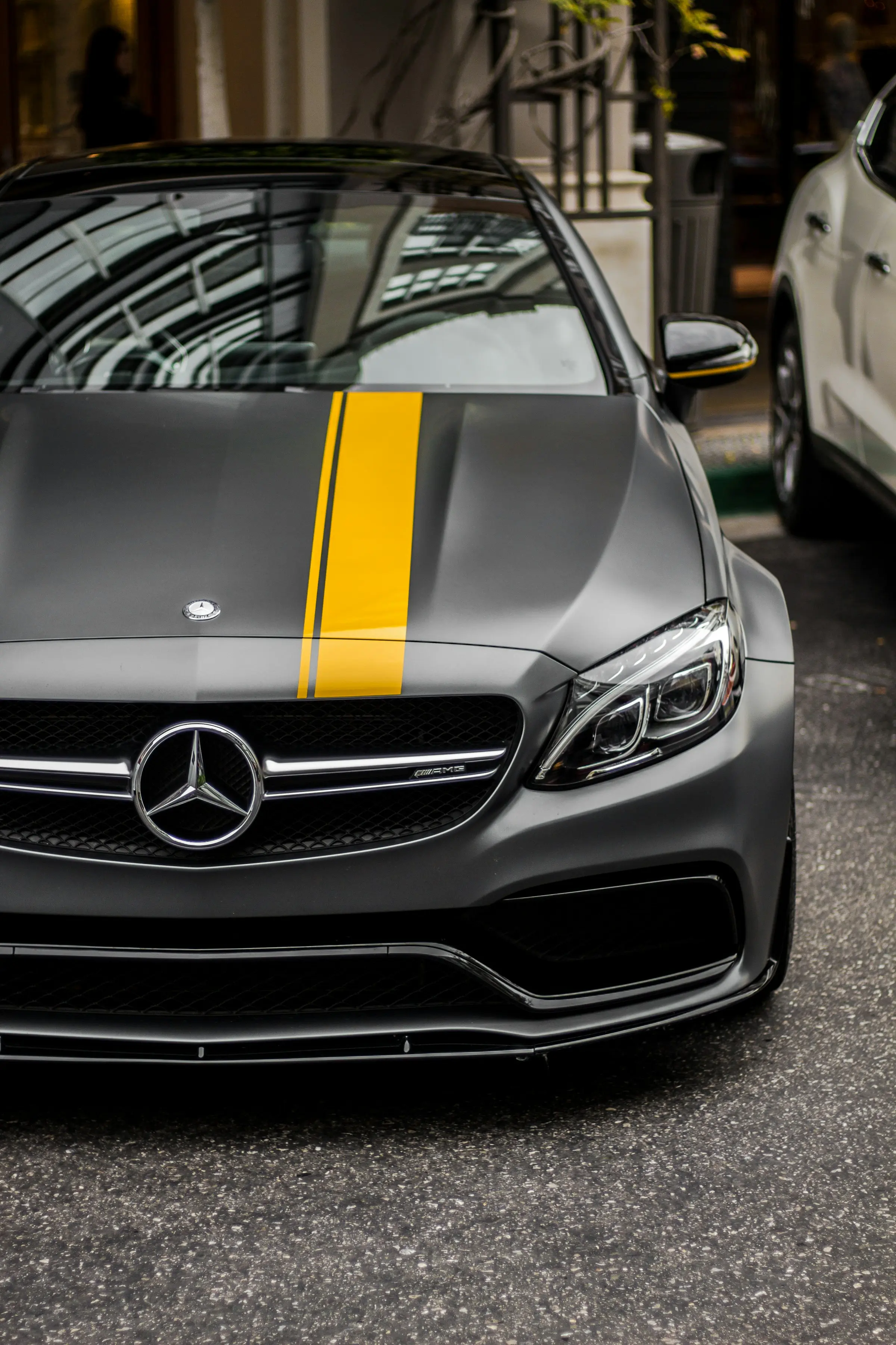 Close view of a grey Mercedes-AMG bonnet with a yellow stripe, reflecting the street