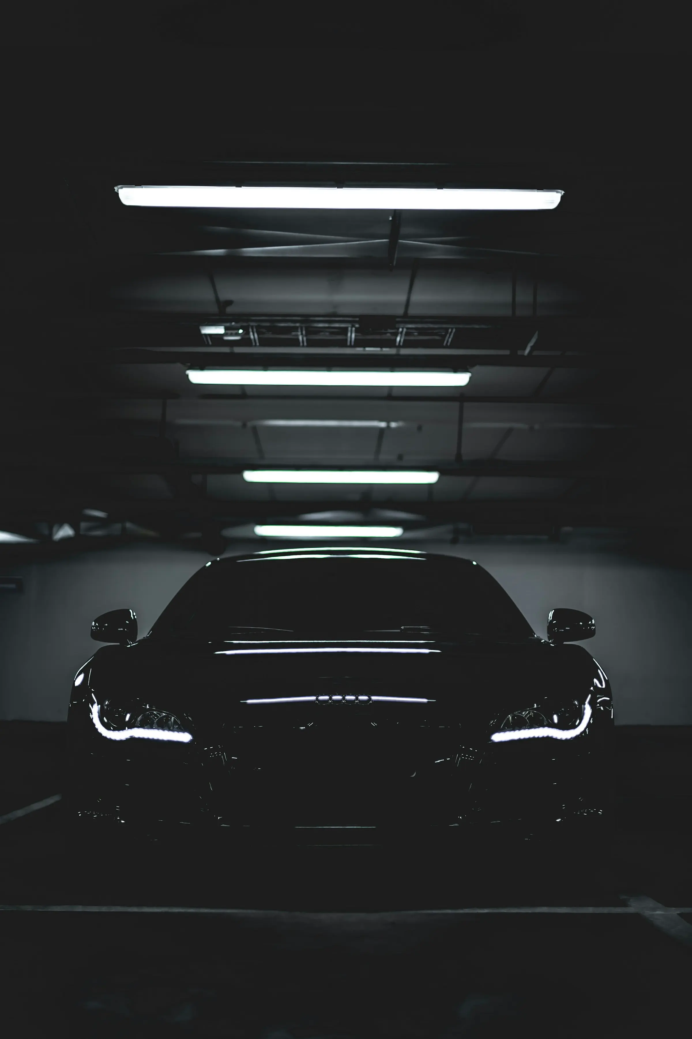 A black performance car under rows of fluorescent strip lights in a dark studio