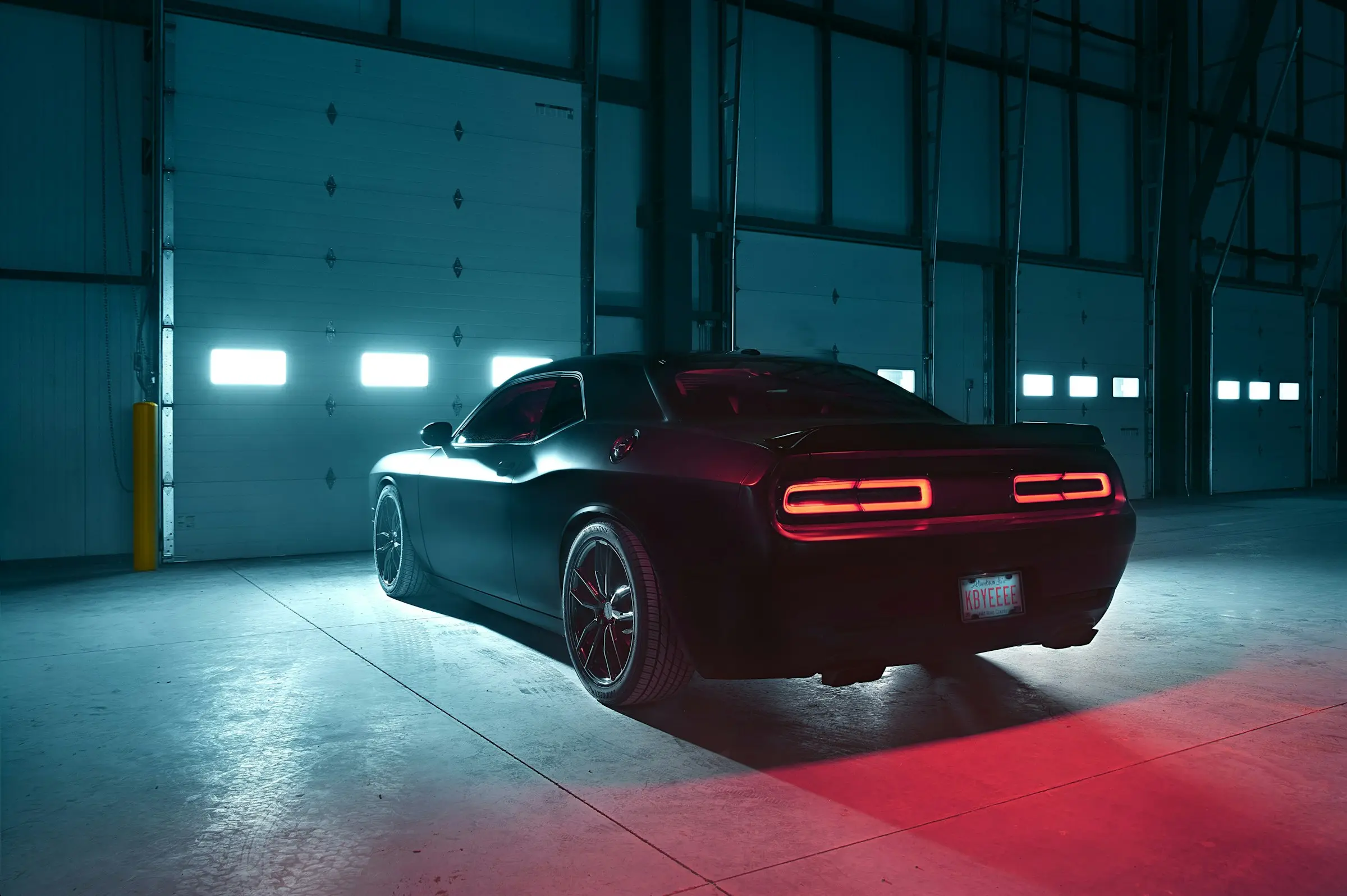 A dark coupé lit by cool studio light in a hangar-style workshop