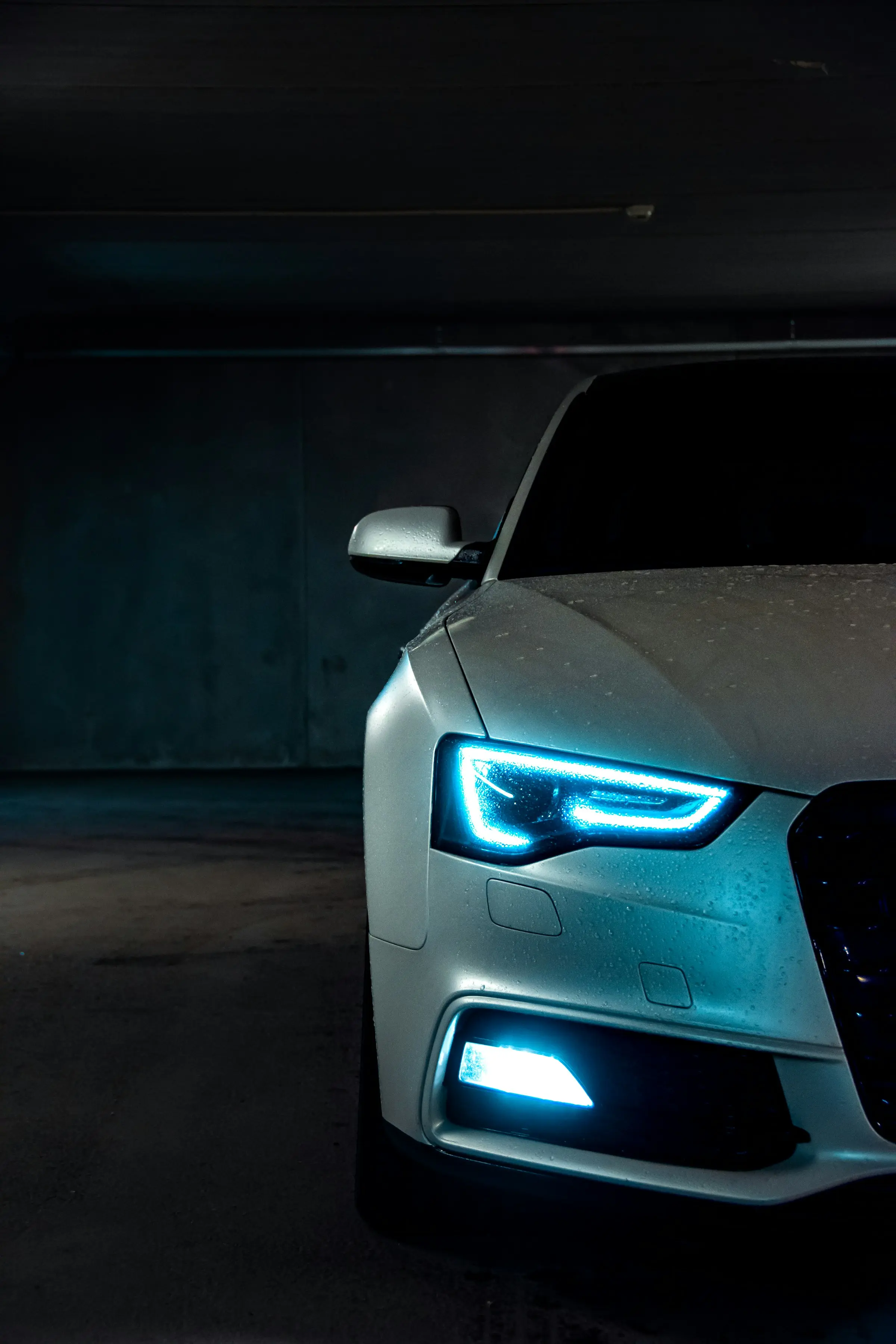 Close detail of a pale car's LED headlight glowing blue in a dark workshop