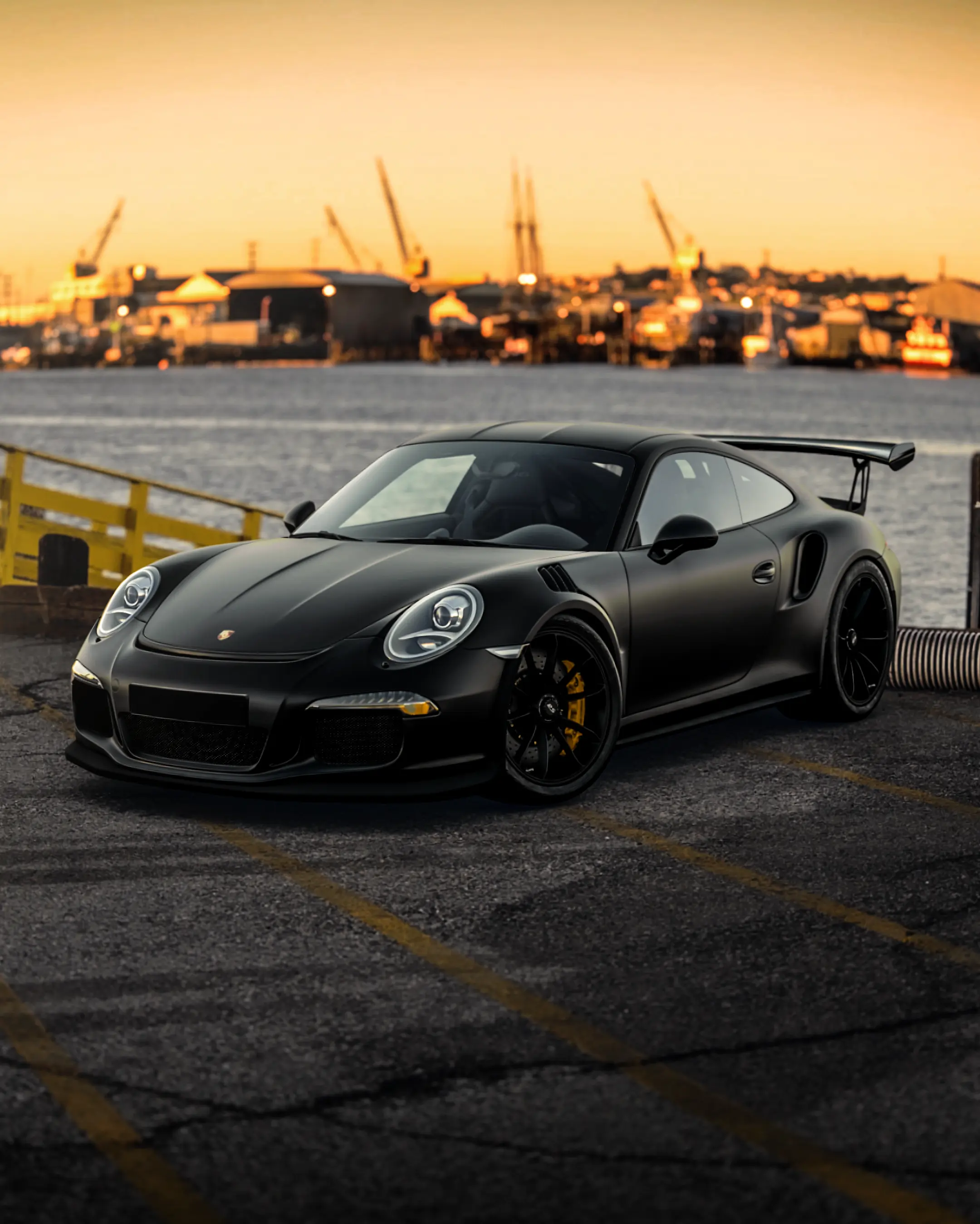 Matte black Porsche 911 GT3 RS parked on a harbour quay at sunset