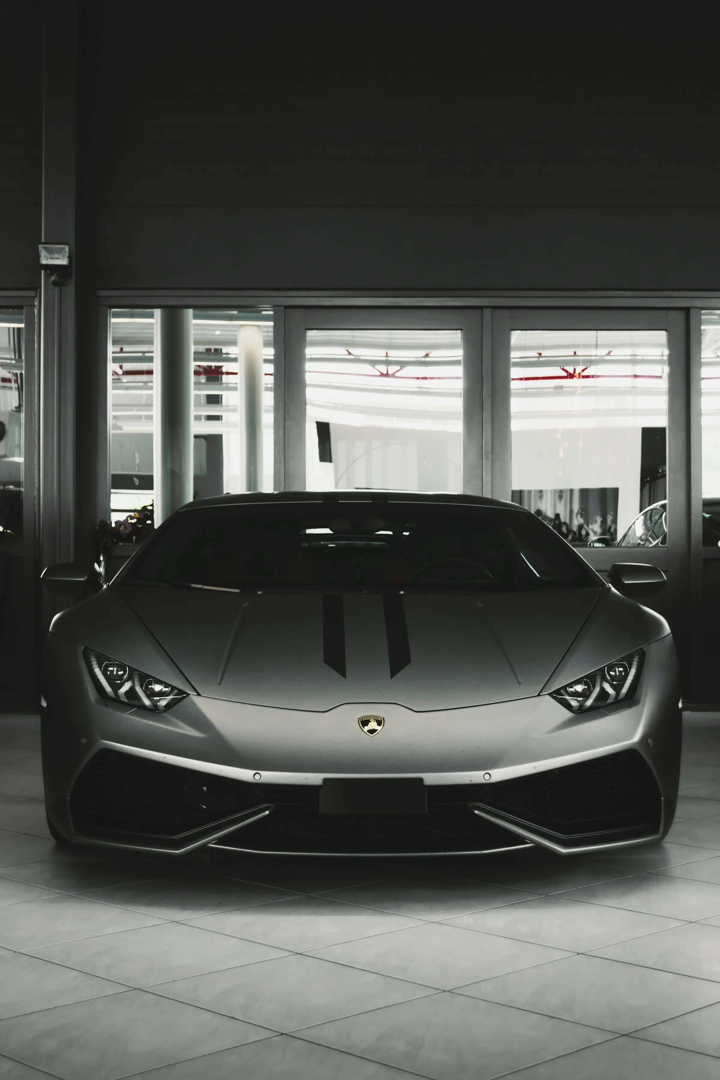 Grey supercar photographed head-on in a bright glass showroom, in monochrome